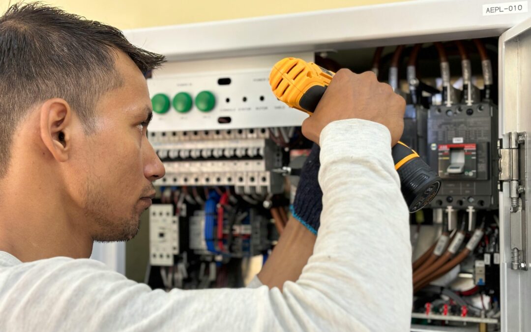 Electrician using a screwdriver to perform maintenance on an electrical panel with various switches and wiring.