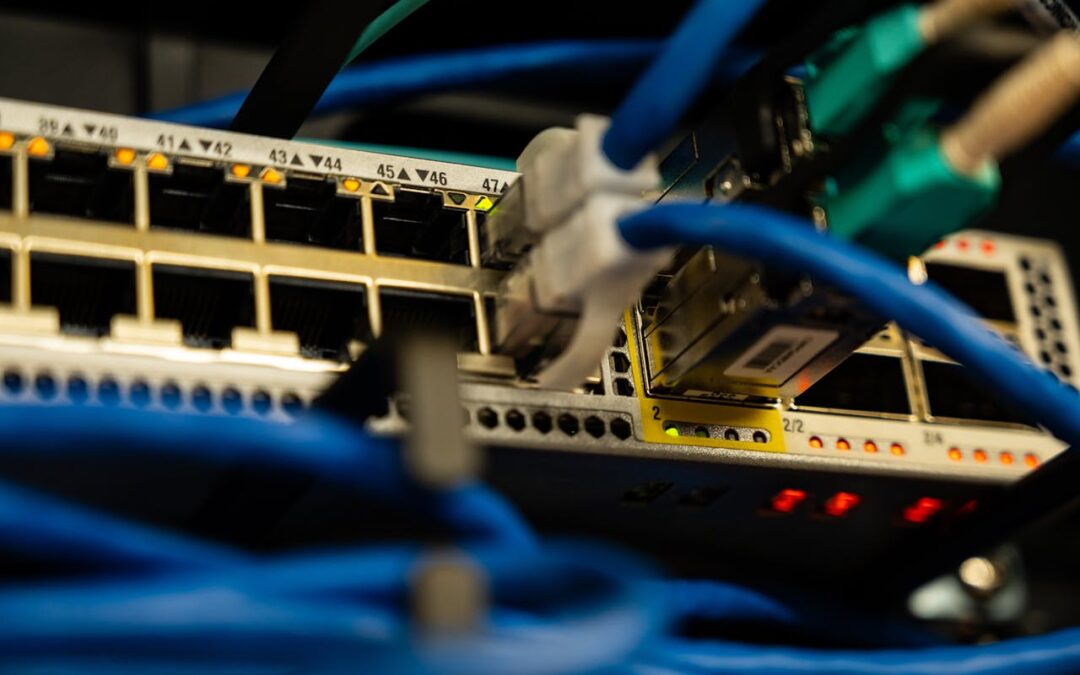 Close-up of a network switch with multiple Ethernet cables connected, featuring illuminated indicator lights considered a electrical upgrade and a focus on blue and green cable connectors.